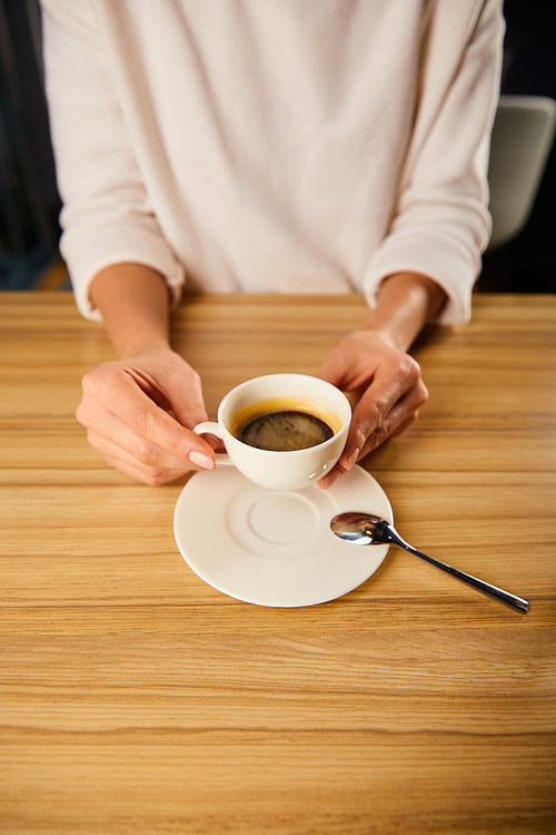 cropped view of woman holding cup of coffee in cafe