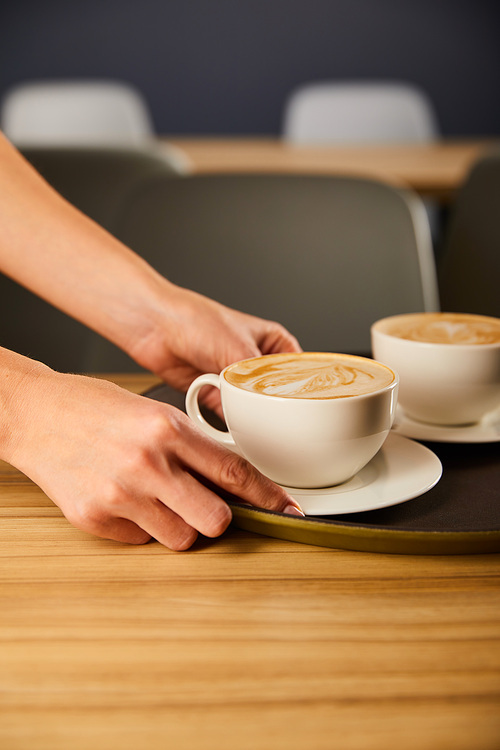 cropped view of woman holding saucer with cup of cappuccino