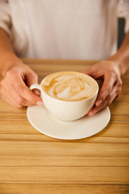 cropped view of woman holding cup with cappuccino