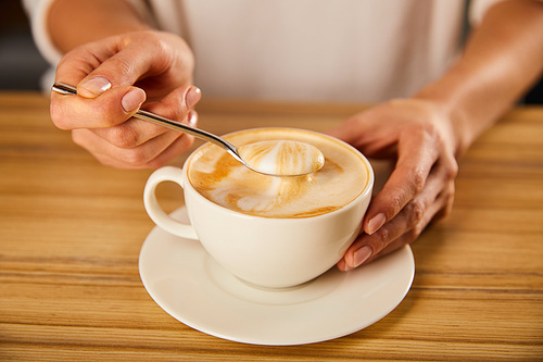 selective focus of woman holding spoon with cappuccino foam