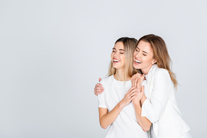 happy mother hugging young daughter with closed eyes isolated on grey
