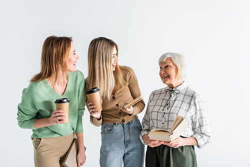 three generation of happy women holding paper cups and books isolated on white