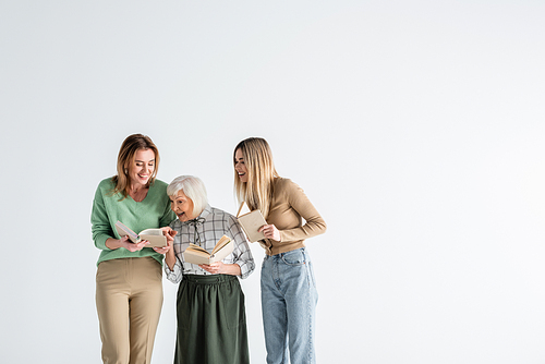 three generation of happy women holding books and smiling isolated on white