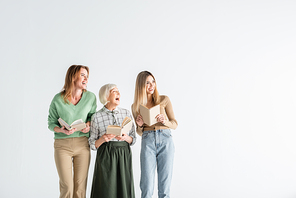 three generation of happy women holding books and looking away isolated on white