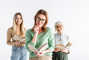 three generation of smiling women in glasses reading books isolated on white