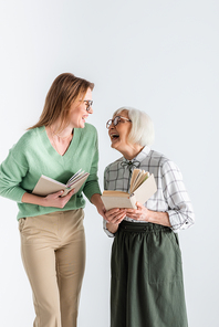 senior mother laughing with daughter in glasses while holding books isolated on white