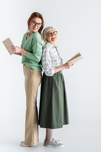 full length of senior woman and daughter in glasses holding books on white