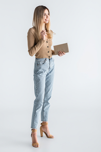 full length of happy young woman holding book and glasses on white