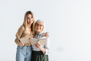 happy young woman hugging granny in glasses and holding books isolated on white
