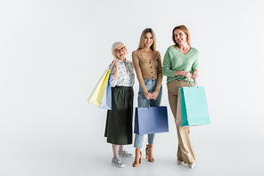 full length of three generation of cheerful women holding shopping bags on white