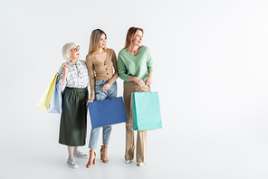 full length of three generation of happy women holding shopping bags and looking away on white