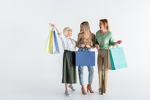 full length of three generation of joyful women holding shopping bags on white