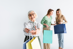 cheerful senior woman holding shopping bags near daughter and granddaughter on blurred background