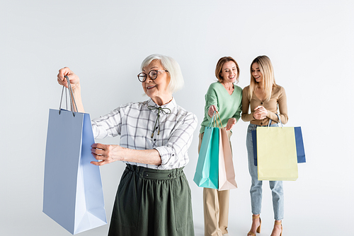 happy senior woman holding shopping bags near daughter and granddaughter on blurred background