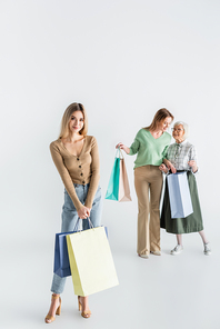 full length of happy young woman standing with shopping bags near mother and granny on blurred background