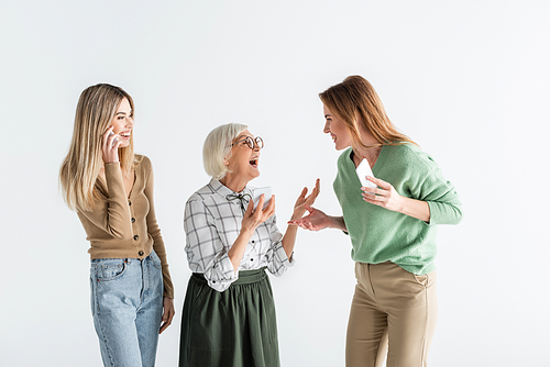 three generation of amazed women holding smartphones and looking at each other isolated on white