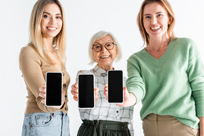 three generation of happy women holding smartphones with blank screen isolated on white