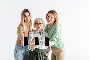 three generation of cheerful women holding smartphones with blank screen isolated on white