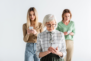 senior woman in glasses using smartphone near daughter and granddaughter on blurred background