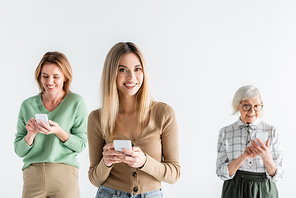 happy young woman standing with smartphone near mother and granny on blurred background isolated on white