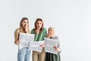 three generation of shocked women holding newspapers isolated on white