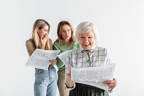 cheerful senior woman reading newspaper near daughter and granddaughter on blurred background isolated on white