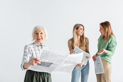 cheerful senior woman holding newspaper near daughter and granddaughter on blurred background isolated on white
