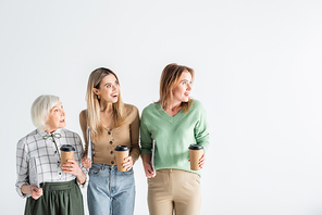three generation of amazed women holding newspapers and paper cups isolated on white