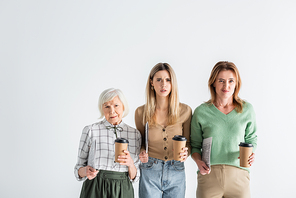 three generation of dissatisfied women holding newspapers and paper cups isolated on white