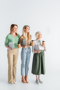 full length of three generation of happy women holding newspapers and paper cups on white