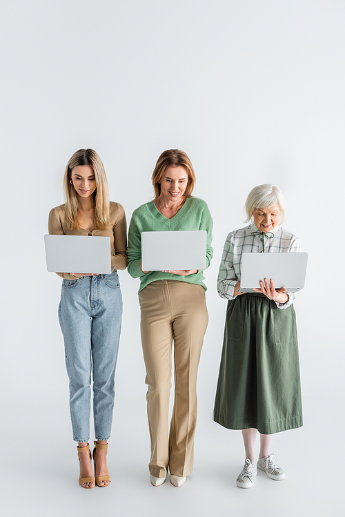 full length of three generation of happy women using laptops on white