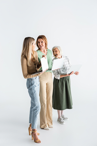 full length of three generation of women holding laptops and smiling on white