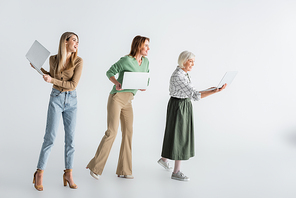 full length of three generation of joyful women holding laptops on white