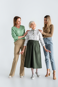 full length of women looking at cheerful senior woman on white
