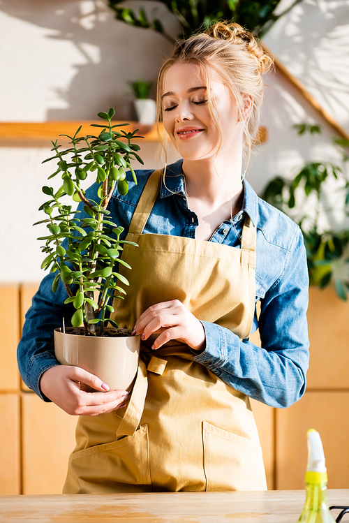 cheerful young woman with closed eyes holding plant in flowerpot