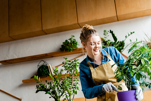 happy woman in gloves transplanting plant in flowerpot