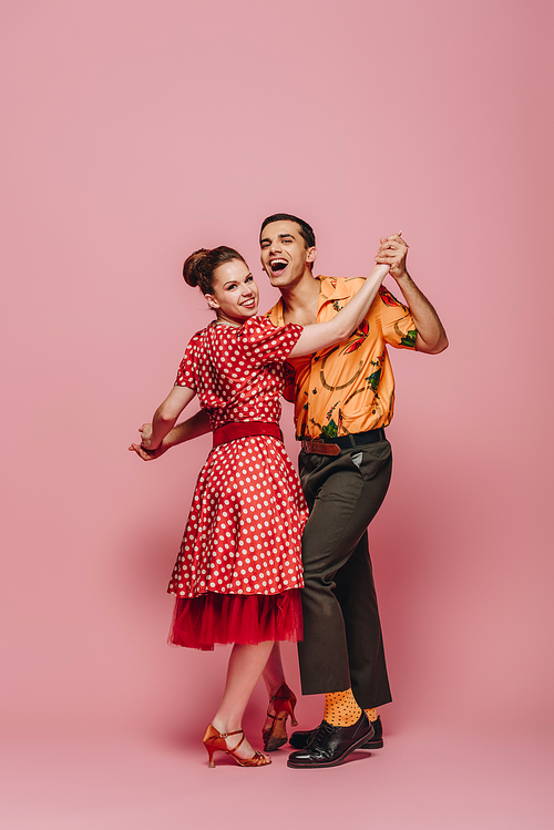 stylish dancers holding hands while dancing boogie-woogie on pink background