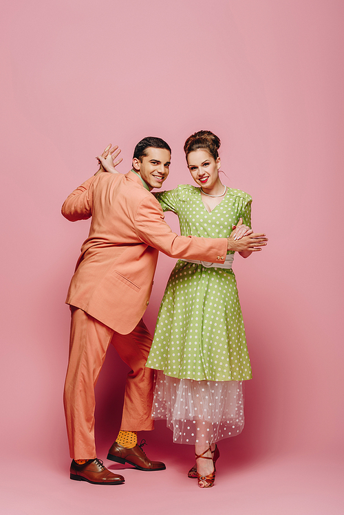 stylish dancers holding hands while dancing boogie-woogie on pink background