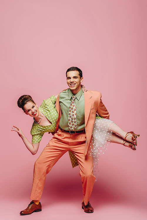 elegant dancer holding girl while dancing boogie-woogie on pink background