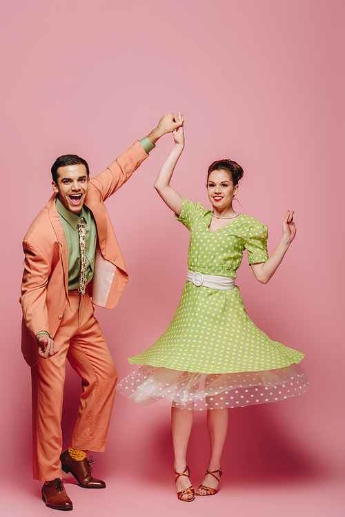 cheerful dancers holding hands while dancing boogie-woogie on pink background