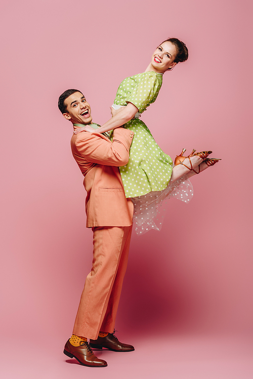 stylish dancer holding girl while dancing boogie-woogie on pink background
