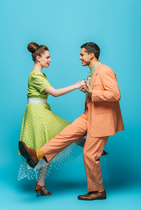 side view of stylish dancers holding hands while dancing boogie-woogie on blue background