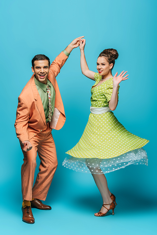 stylish dancers holding hands while dancing boogie-woogie on blue background