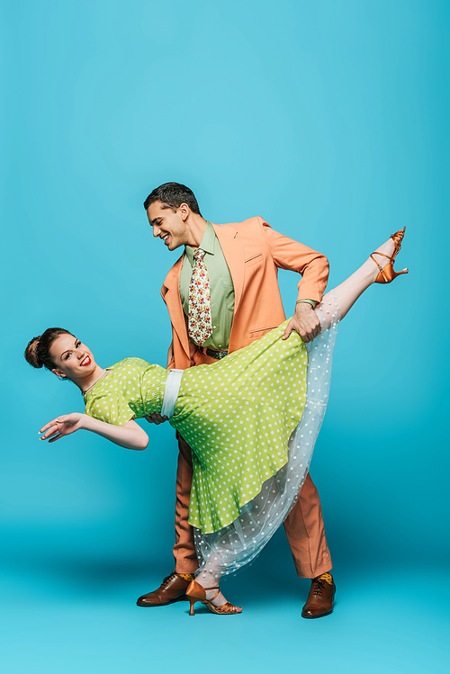 stylish dancer supporting girl while dancing boogie-woogie on blue background