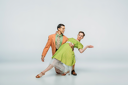 handsome dancer standing on knee and supporting partner while dancing boogie-woogie on grey background