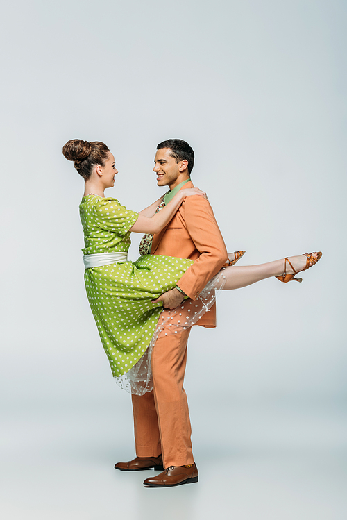 handsome dancer holding girl while dancing boogie-woogie on grey background
