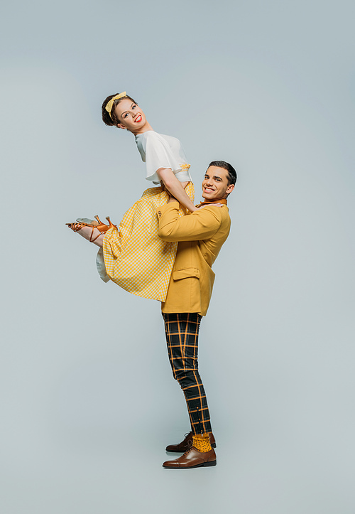 happy dancer holding girl while dancing boogie-woogie on grey background