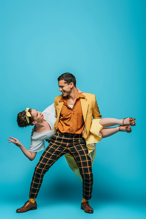 handsome dancer holding girl while dancing boogie-woogie on blue background