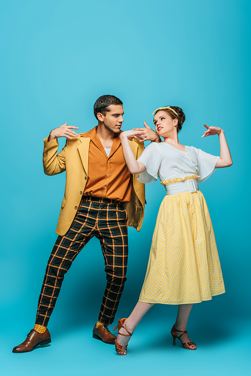 stylish dancers looking at each other while dancing boogie-woogie on blue background