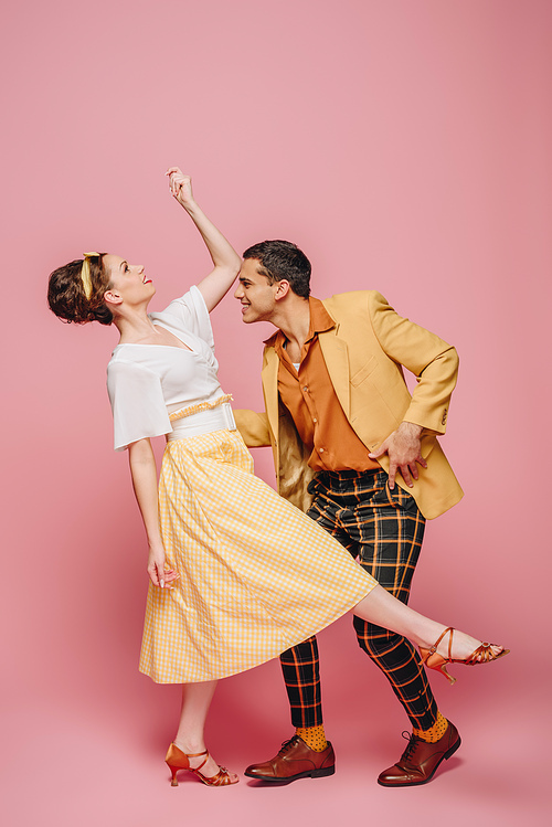 side view of stylish dancers dancing boogie-woogie on pink background